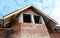 A close-up on attic, mansard and roofing construction with unfinished soffit, eaves, fascia and window of a brick house