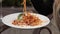 Close-up attractive female hand eating tasty fresh pasta from white big plate using fork