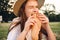 Close up attractive girl in straw hat emotionally eating baguette bread on picnic in park