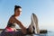 Close-up of attractive sportswoman holding leg on handrope, stretching on the seaside promenade. Female runner warming