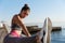 Close-up of attractive sportswoman holding leg on handrope, stretching on the seaside promenade. Female runner warming