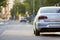 Close-up back view of new shiny expensive silver car moving along city street on blurred trees, cars and buildings background on