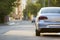 Close-up back view of new shiny expensive silver car moving along city street on blurred trees, cars and buildings background on