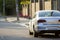 Close-up back view of new shiny expensive silver car moving along city street on blurred trees, cars and buildings background on