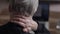 Close-up back view of unrecognizable gray-haired mature business man sitting at workplace experiences severe pain in