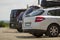 Close-up back view of white expensive modern car with black trunk on roof on blurred background of row of cars and vans parked on