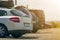 Close-up back view of white expensive modern car with black trunk on roof on blurred background of row of cars and vans parked on