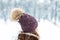 Close-up back view of young adult woman head wearing warm stylish woolen knitted handmade hat with big fluffy natural fur pompon.