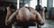 Close-up back view young Caucasian muscular man lying on bench lifting dumbbells in large gymnasium hall slow motion.