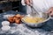 Close-up of a baker mixing eggs with a hand blender in a steel bowl