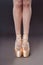 Close-up of Ballerine feet in pointe shoes on grey background. Ballerina is standing on the hips. Studio shot of ballerina legs in