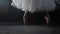 Close up of ballet dancer as she practices exercises on dark stage or studio. Woman`s feet in pointe shoes. Ballerina