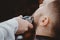 Close-up of barber shearing beard to man in barbershop electric razor