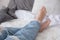 Close-up of barefoot attractive female legs dressed blue jeans in bed, home relaxation and rest