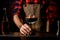 Close-up. Barman`s hand holds black frosted glass with piece of ice