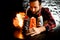 Close-up bartender holds black ceramic glass with slice of citrus and make fire