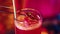 Close-up. Bartender making sweet cocktail, decorating drink with dry orange slice. Neon colored bar