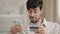 Close-up bearded arabic business man in glasses with credit card and phone makes purchase online shopping enters bank