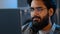 Close-up bearded male face reflection light from laptop monitor in glasses. Busy serious focused Arab Indian man looking