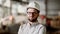 Close up of bearded man in white shirt, protective helmet and eyeglasses standing in construction area. Young architect