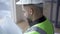 Close-up of bearded worker in helmet and green jacket reading documents. Professional builder with building drawings in