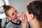 Close-up of a beautician wearing colorful protective mask during COVID-19 while applying make up on beautiful young woman who\'s si