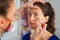 Close-up of a beautician wearing colorful protective mask during COVID-19 while applying make up on beautiful young woman who\'s si