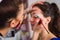 Close-up of a beautician wearing colorful protective mask during COVID-19 while applying make up on beautiful young woman who\'s si