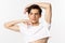 Close-up of beautiful androgynous man in crop top posing for camera, standing against white background