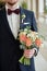 Close up of beautiful bridal bouquet of coral roses and greenery in groom& x27;s hand indoors, copy space.