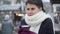 Close-up of beautiful Caucasian woman in white scarf drinking coffee outdoors. Frozen young girl with brown eyes