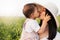 Close up beautiful portrait of a pretty mother with hat embraces and kiss a daughter, toddler, baby, on nature, field background.