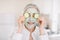 Close up of beautiful retired woman with facial mask on her face holding slices of fresh cucumber covering her eyes, on