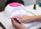 Close-up beautiful woman hands and lamp for nails on table. Nail gel salon.