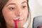 Close up of a beautiful young woman using a shaver pretending to shave her mustache looking at small mirror, in a bath