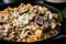 Close-up of beef stroganoff being served from a cast iron skillet, with steam rising from the creamy sauce