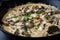 Close-up of beef stroganoff being served from a cast iron skillet, with steam rising from the creamy sauce