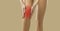 Close up on beige background woman holding sore knee where focus of pain is marked in red.