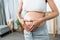 Close-up. Belly of pregnant teenage mother standing in living room and hands forming a heart shape on her belly.