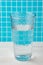close-up of big glass of water on white table and blue and white mosaic background, vertically,