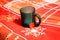 Close-up of a black ceramic cup with a teabag on a red blanket