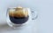 Close up black coffee with natural foam in double walled transparent glass with plain background, morning boost, espresso,