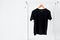 Close up of black color t-shirt hanging on wooden cloth hanger on clothing rack over white background, copy space