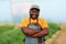 Close-up of black farmer standing in a greenhouse, crops in background, smiling.