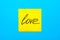 Close up black handwritten inscription love on one yellow square sticker on blue background with copy spase