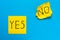 Close up black handwritten inscription yes and no word on two yellow square stickers on blue background with copy spase,