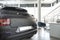 Close-up of black mat car in the foreground and office desk with chair in the background standing in bright car showroom interior