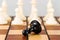 Close-up of a Black pawn lying on a chessboard and surrounded by white pieces. Other chess pieces in the background.