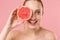Close up blonde half naked woman 20s perfect skin nude make up blue eyes hold in hand grapefruit  on pastel pink