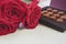 Close up of blooming red roses and elegant box of chocolate truffles. Valentine`s Day or romantic celebration concept.